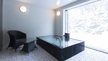 A modern bathroom with a glass-enclosed bathtub, a black chair, and a small table.