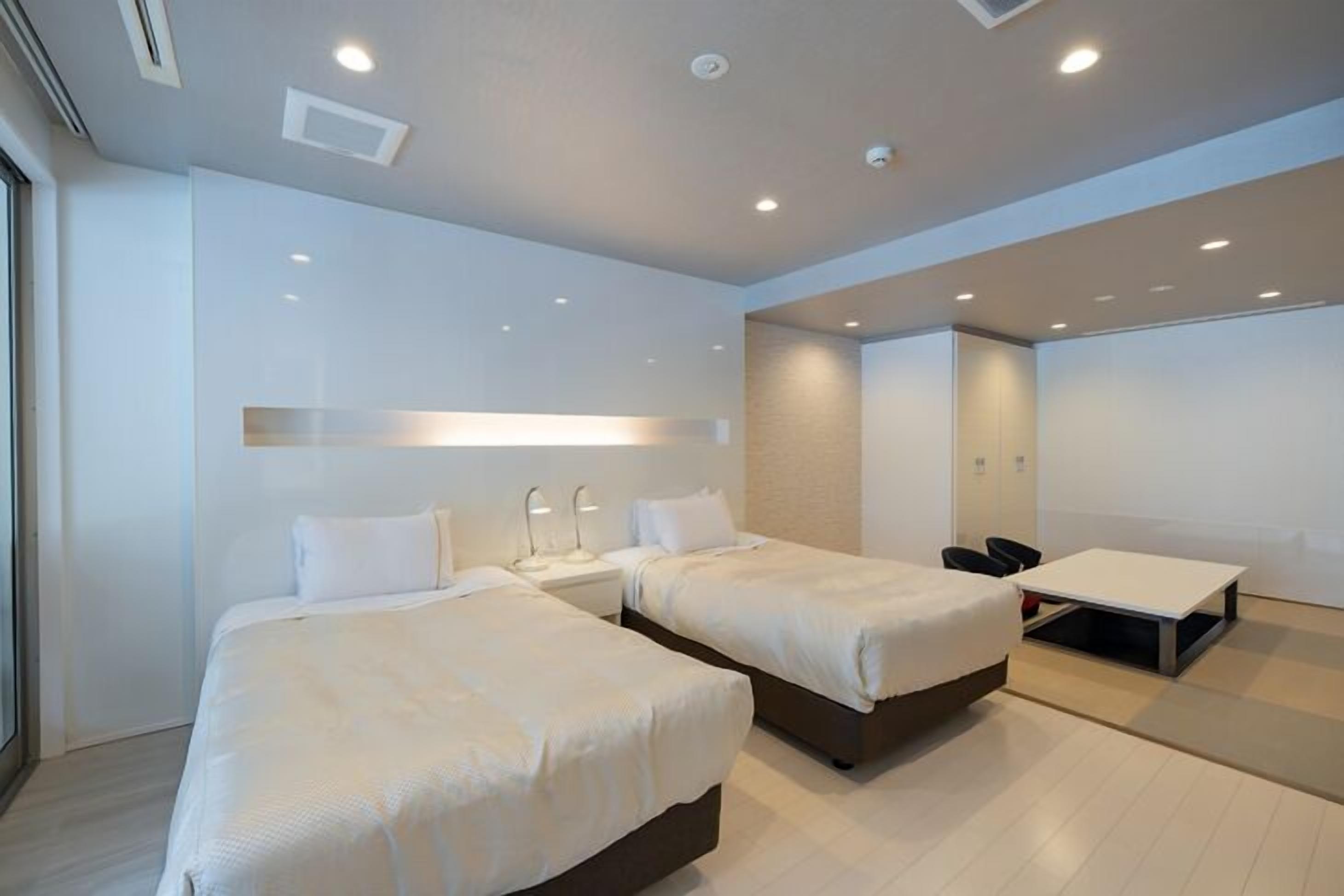 A modern hotel room with two beds, a desk, and a chair.