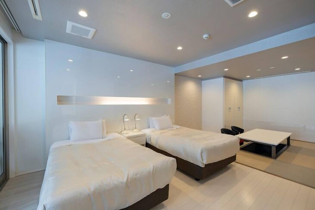 A modern hotel room with two beds, a desk, and a chair.