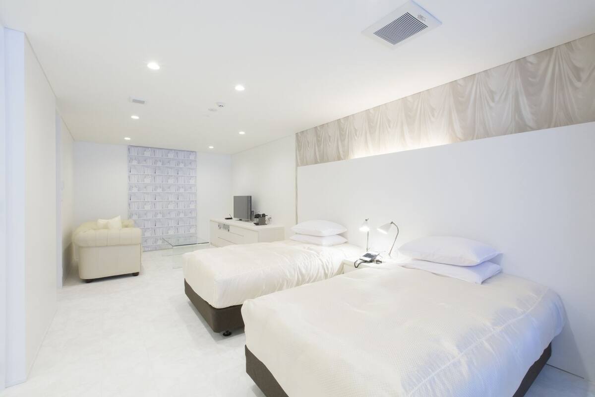 A modern hotel room with two beds, a sofa, a TV, and a bookshelf.