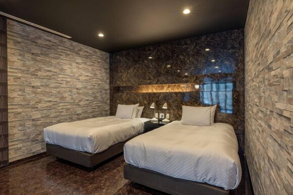 A modern hotel room with two beds, a stone-textured wall, and a night sky view.