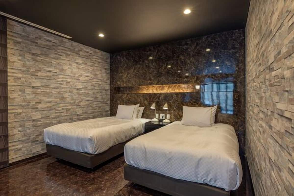 Habitación de hotel moderna con dos camas, una pared con textura de piedra y vistas al cielo nocturno.