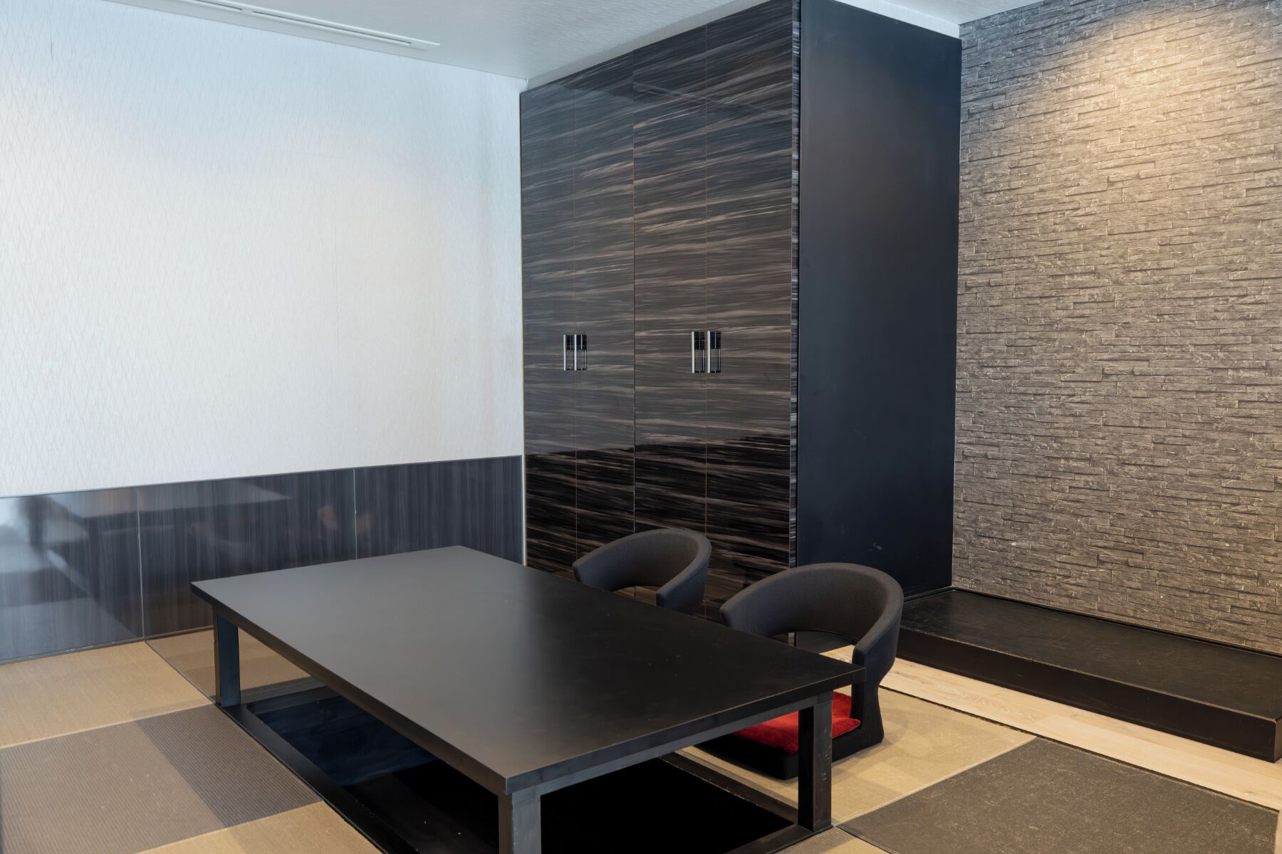Una habitación moderna con un armario de madera oscura, una mesa negra y dos sillas.