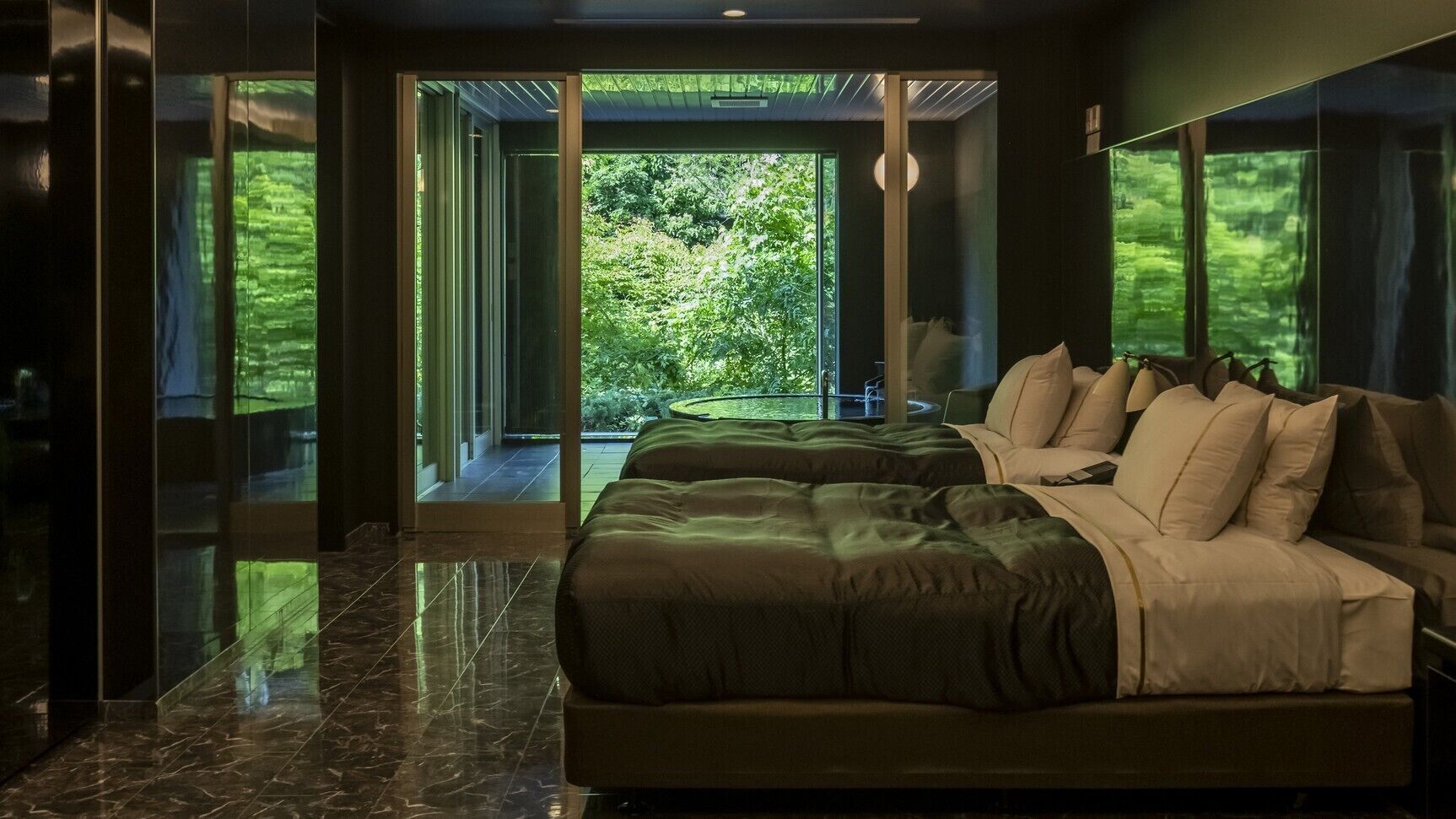 Ein modernes Schlafzimmer mit einem großen Bett, einer Glastür, die auf einen Balkon führt, und Blick ins Grüne.