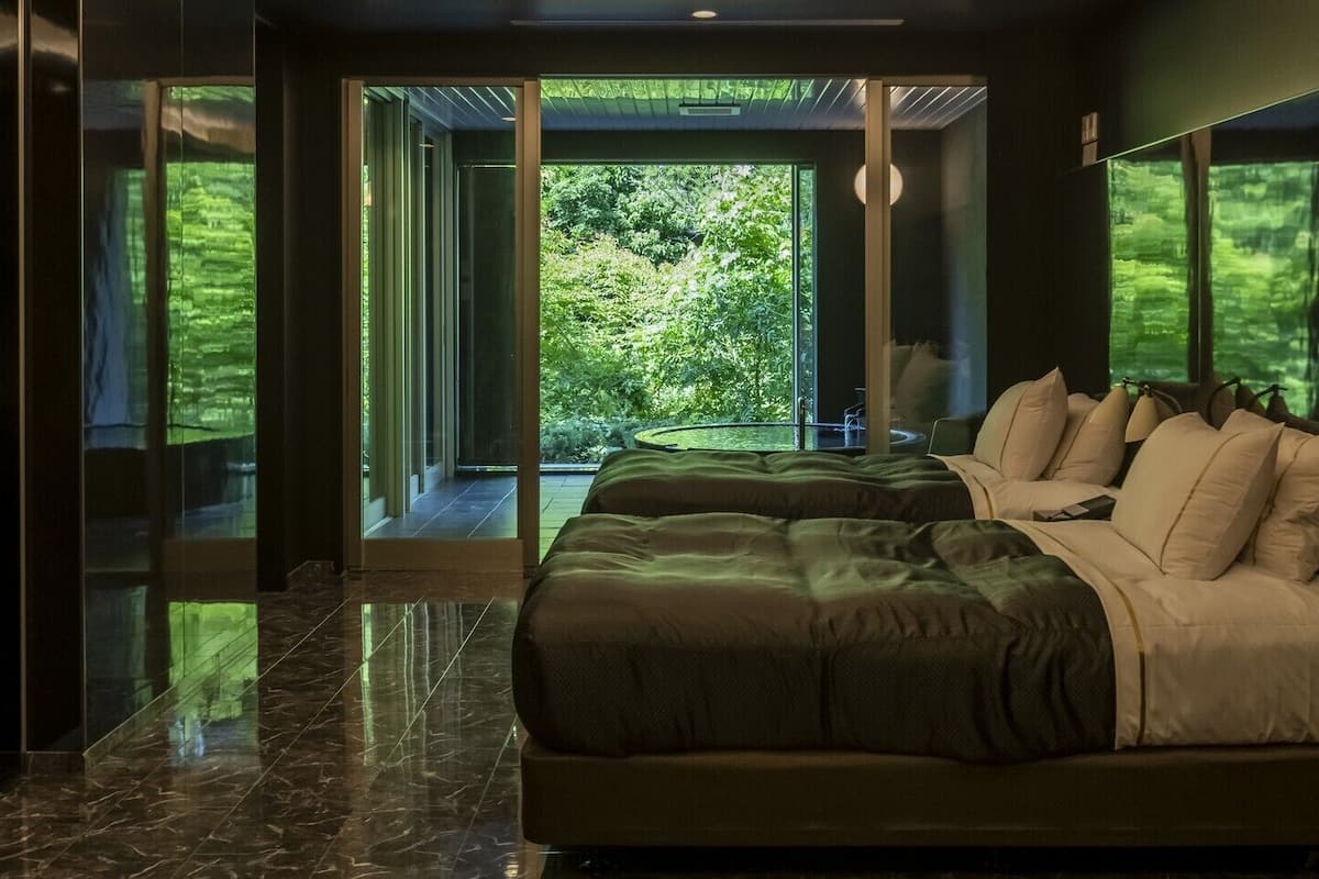 Un dormitorio moderno con una cama grande, un ventanal de vidrio que da a un balcón y vistas a la vegetación.