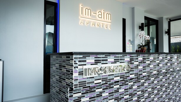 Um balcão de receção com design moderno, com padrão em mosaico de azulejos e uma placa com a inscrição "im-aim APARTMENT".