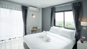 Quarto de hotel moderno com uma cama grande, uma mesa de trabalho e vista para o verde lá fora.