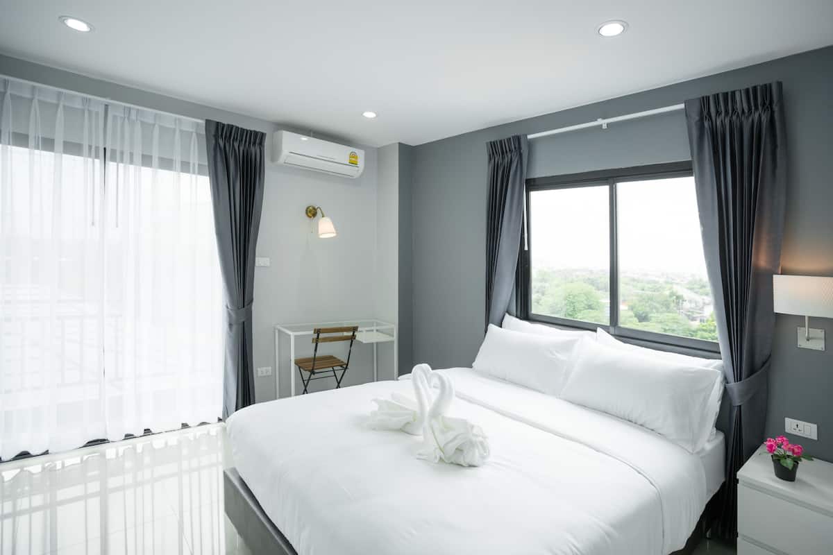 Quarto de hotel moderno com uma cama grande, uma mesa de trabalho e vista para o verde lá fora.