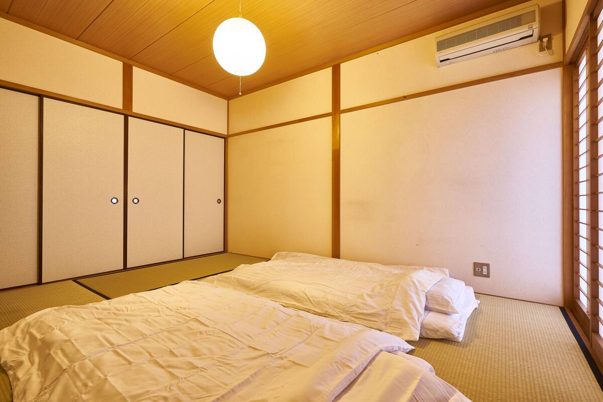 A traditional Japanese room with tatami flooring, a bed with white bedding, and sliding doors.