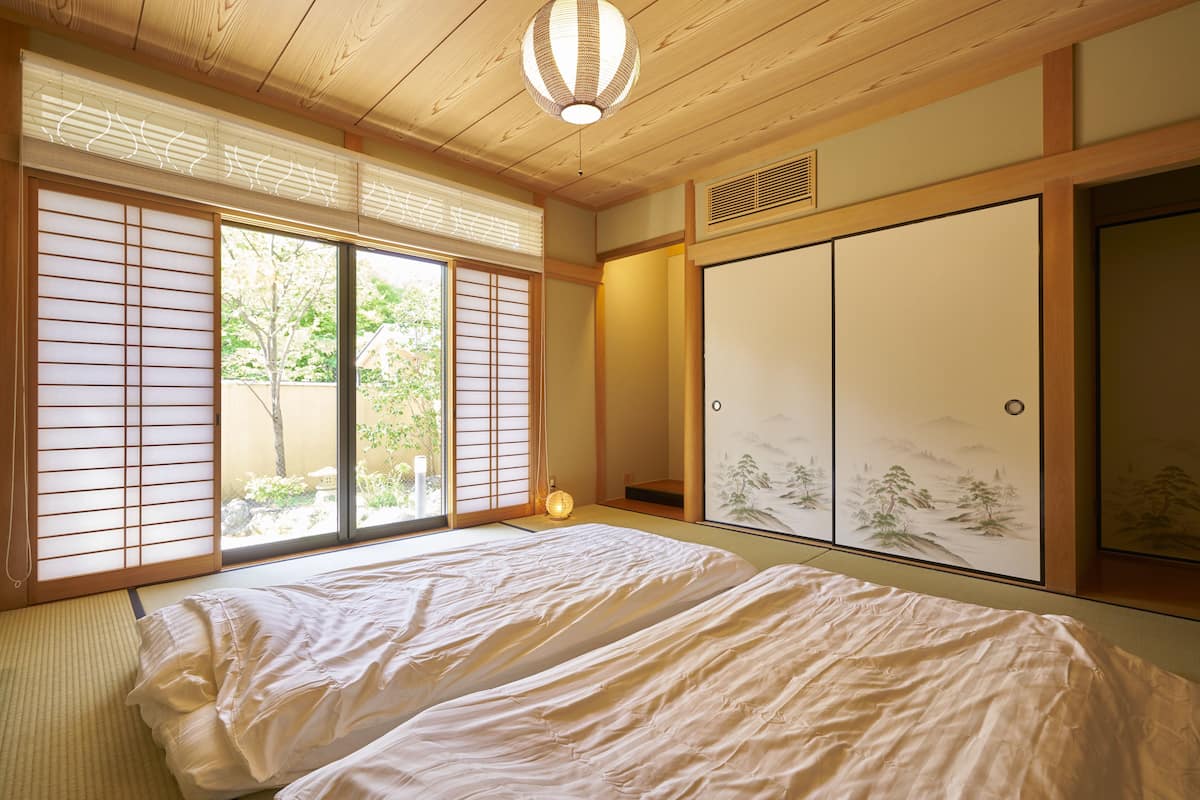 A traditional Japanese room with tatami flooring, sliding doors, and a bed with white bedding.