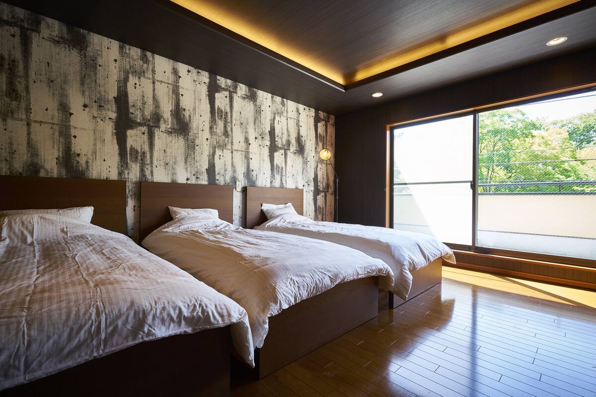 A modern hotel room with two beds, a large window, and a wooden floor.