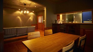 A dining area with a wooden table and chairs, a bench, and a kitchen area with cabinets and a refrigerator. - Nijo Fukuro-Tei (Kyoto)