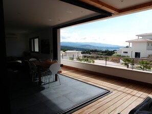 Un salon moderne doté d’une grande fenêtre offrant une vue panoramique sur les montagnes et le paysage urbain.