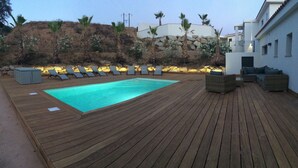 A wooden deck with a swimming pool, lounge chairs, and a small seating area.
