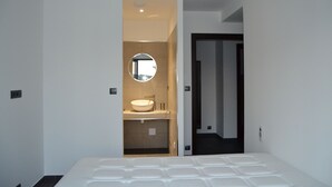A modern bedroom with a large bed, a built-in vanity with a mirror, and a separate bathroom.