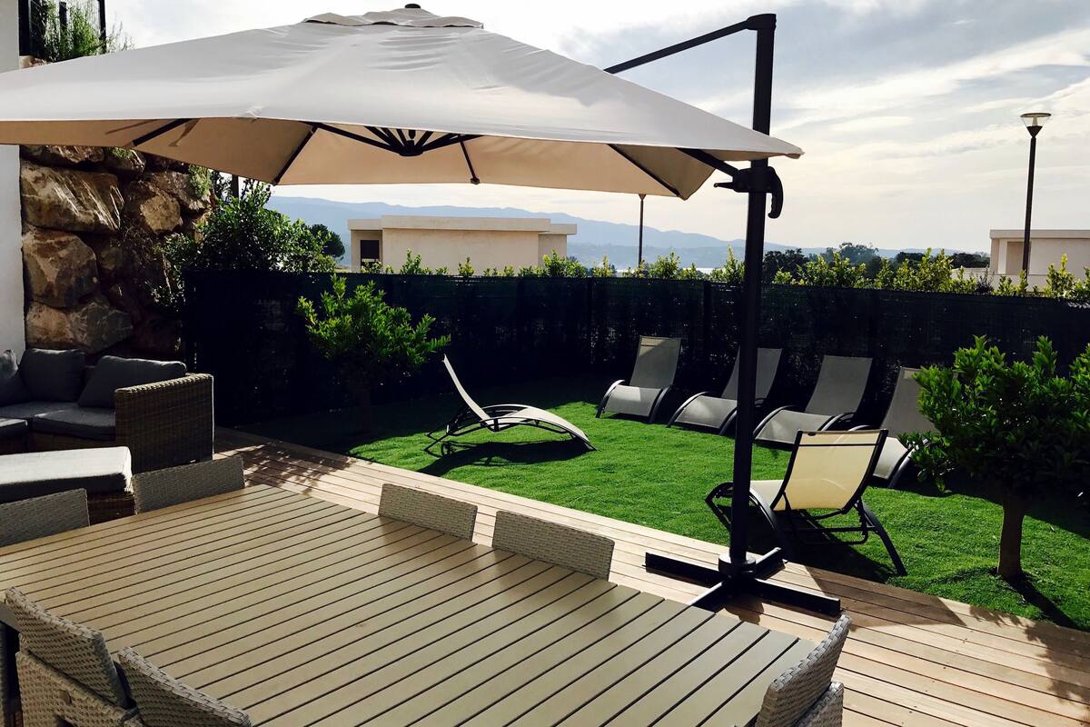 Een terras met een houten dek, tuinmeubilair en een grote parasol voor beschaduwing.