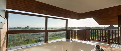 Un balcon spacieux doté d’une grande baignoire blanche, d’une terrasse en bois et offrant une vue imprenable sur un paysage verdoyant.