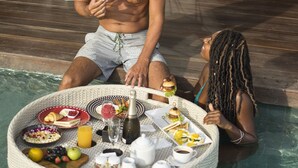 A poolside breakfast setup with a wicker tray containing food, drinks, and a bottle. - Sense Canggu Beach Hotel (Pererenan)