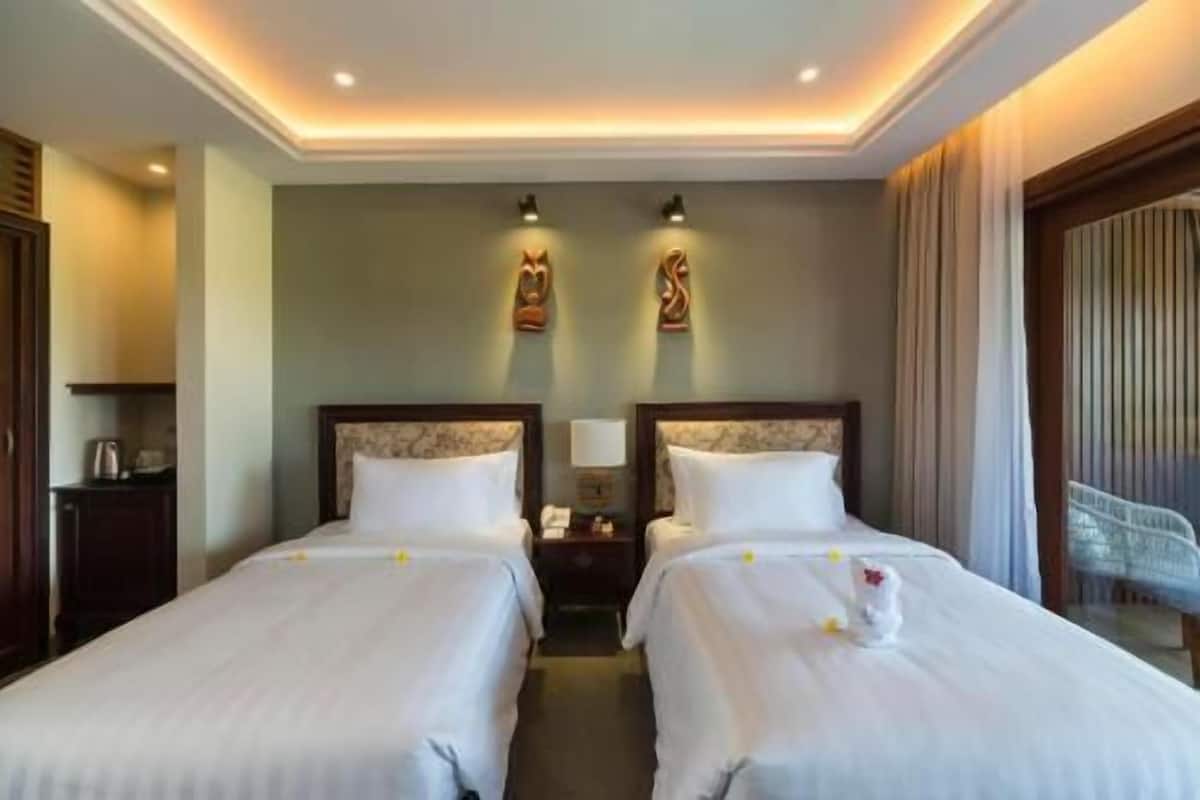 A hotel room with two beds, a desk, a lamp, and a view of the sea.