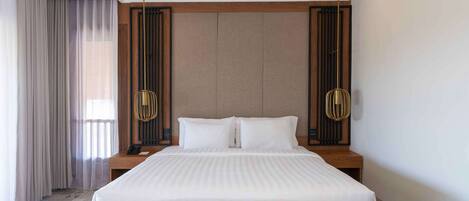 Habitación de hotel con una cama grande, cabecera de madera, mesita de noche y un amplio ventanal con cortinas.