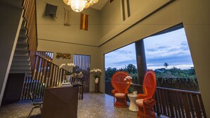 A modern interior with a staircase, a chandelier, and a balcony with a view of the sky and greenery. - Sense Canggu Beach Hotel (Pererenan)