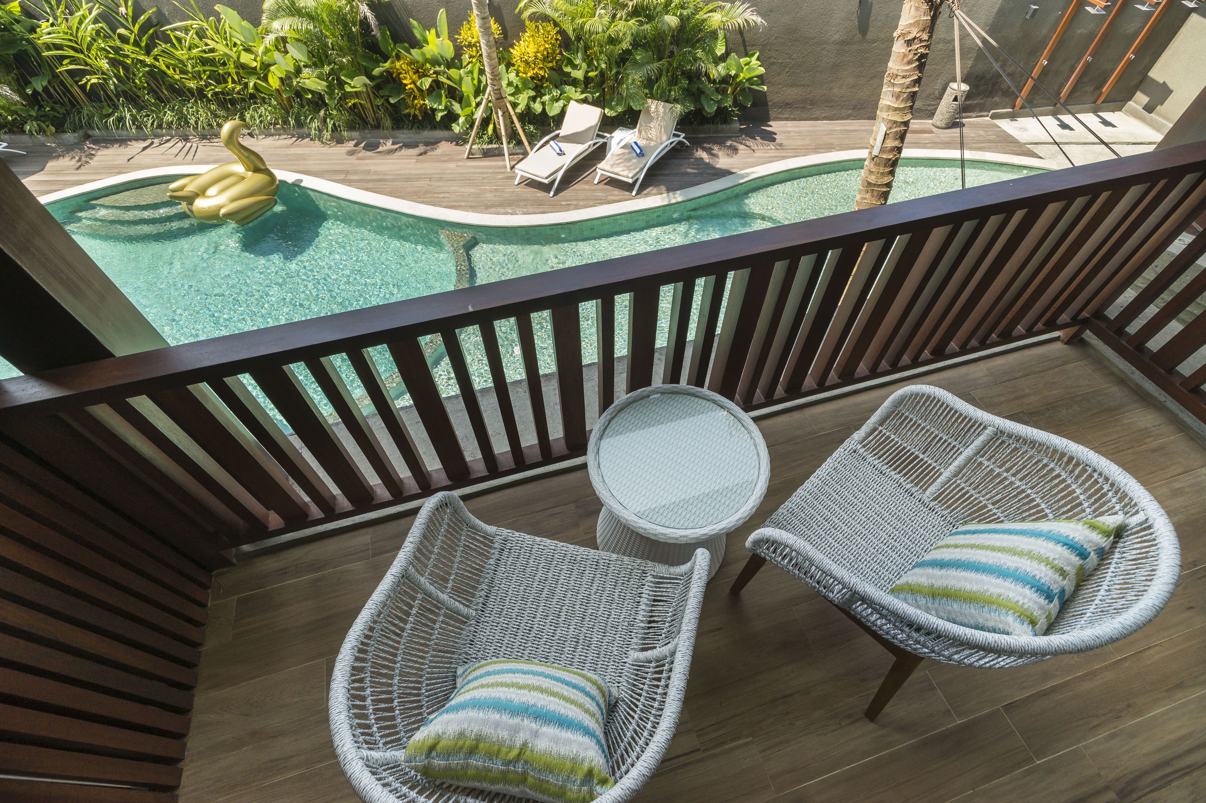 A balcony with two wicker chairs and a small round table, overlooking a swimming pool with lounge chairs and a swan-shaped float.