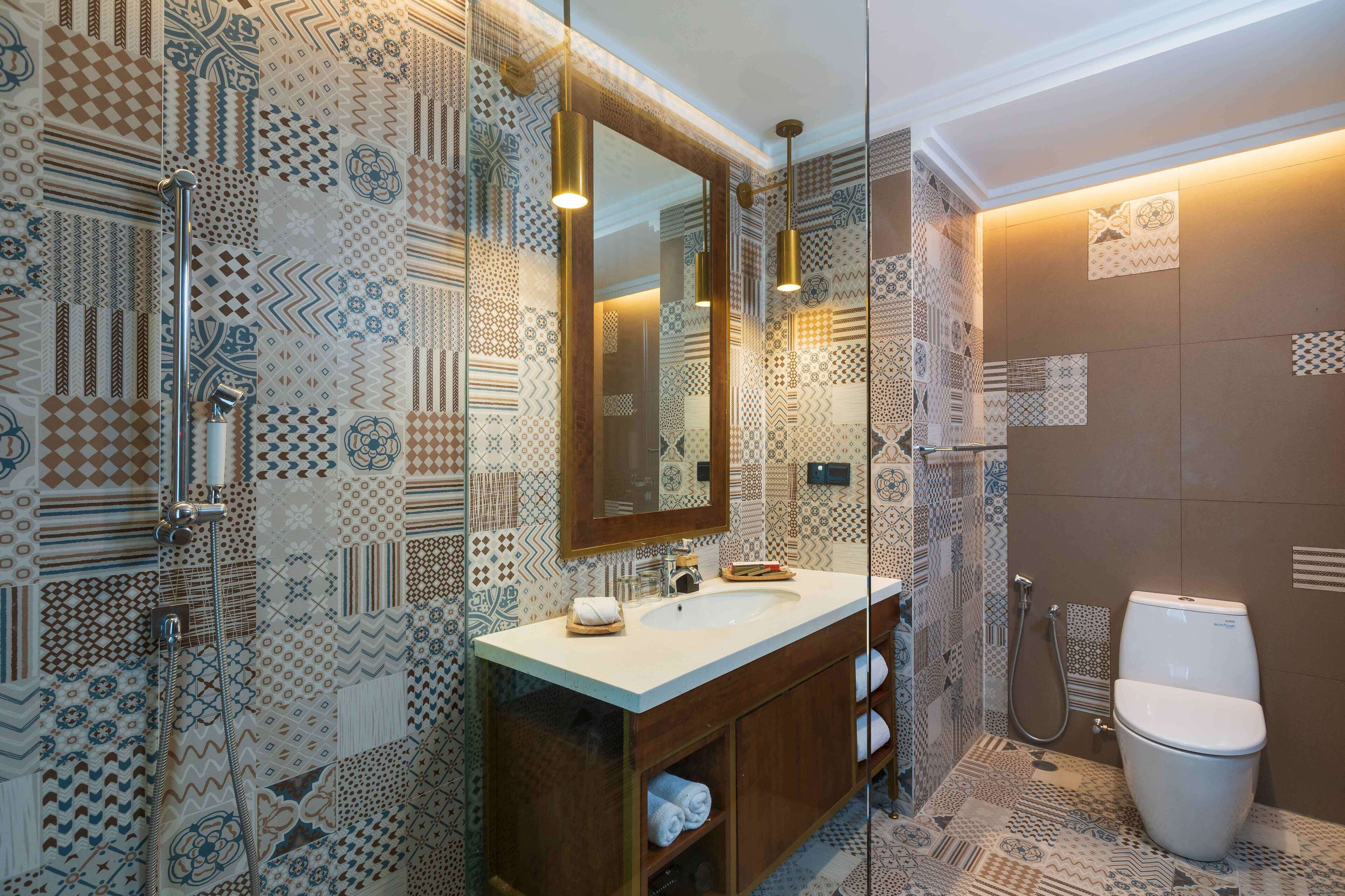 A bathroom with patterned tiles, a wooden vanity, a large mirror, and a toilet.