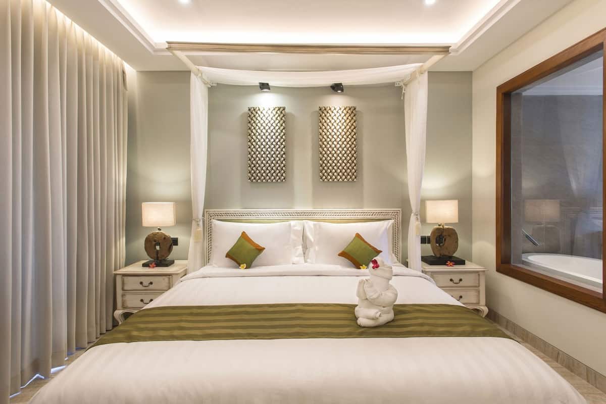 A hotel room with a large bed, two bedside tables, a window, and a decorative wall panel.