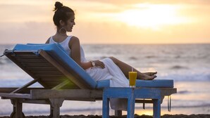 A person relaxing on a beach chair with a drink, overlooking the ocean at sunset. - Sense Canggu Beach Hotel (Pererenan)