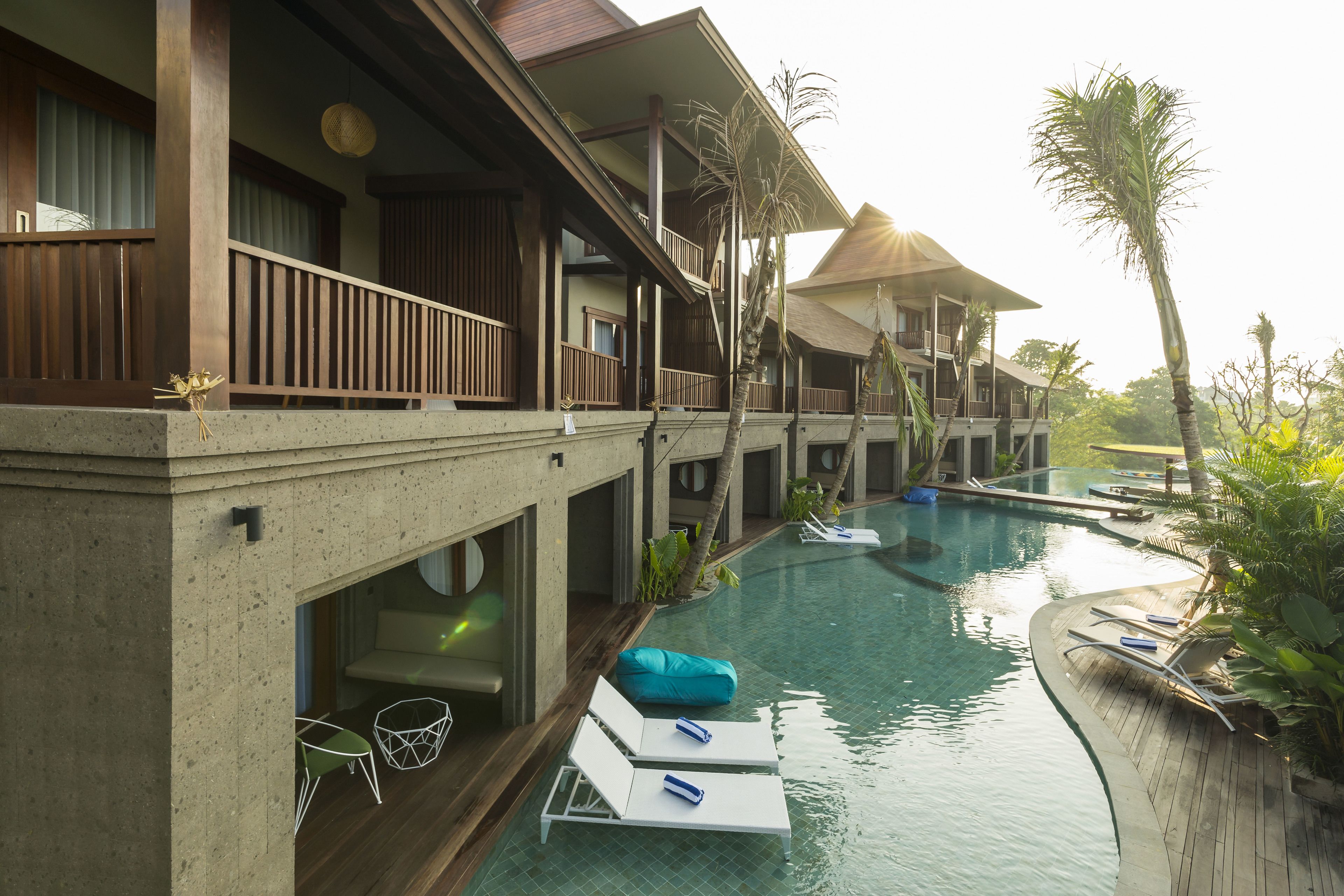 Um resort com várias bangalôs sobre a água, piscina e espreguiçadeiras.