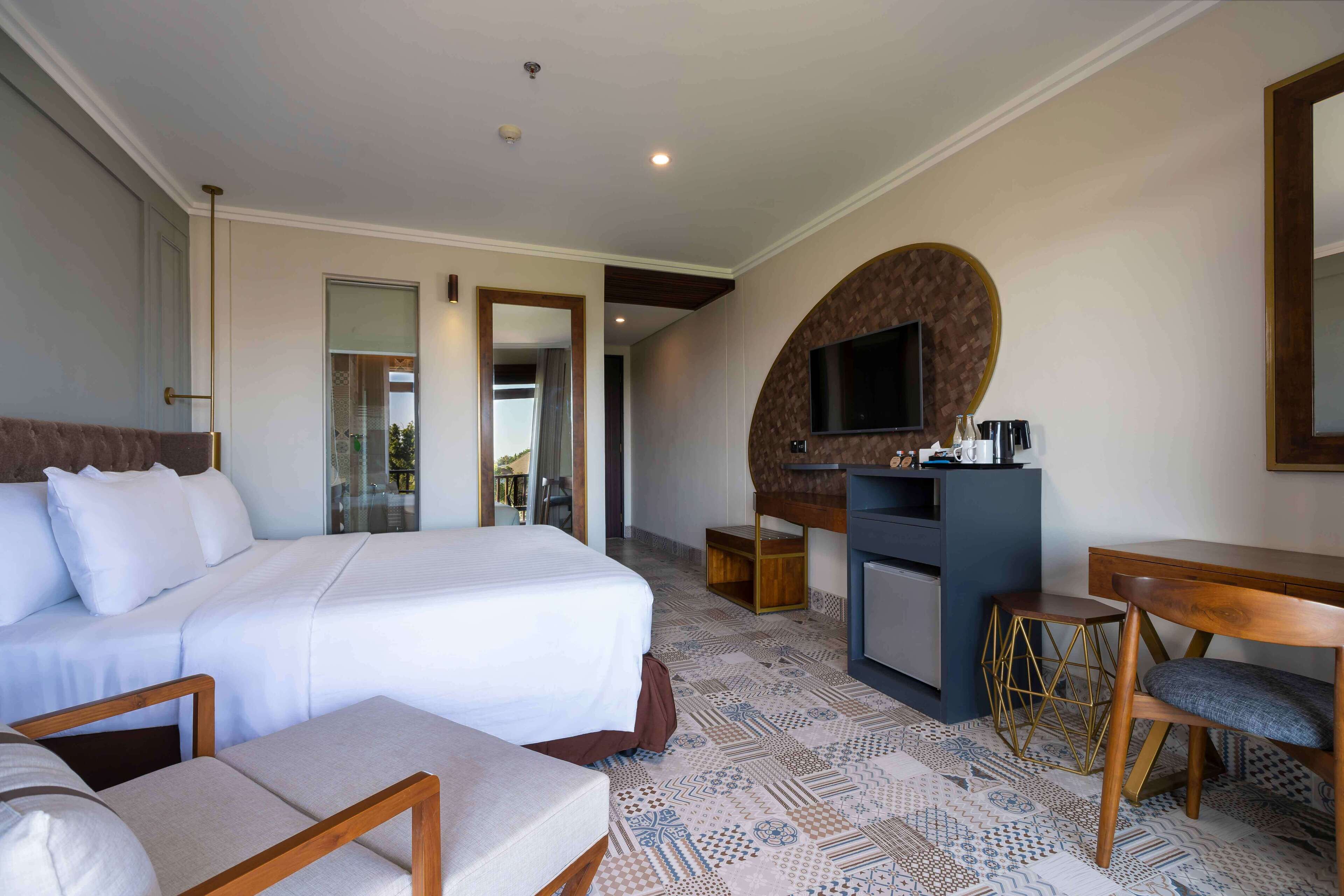A hotel room with a large bed, a desk, a television, and a small kitchenette.