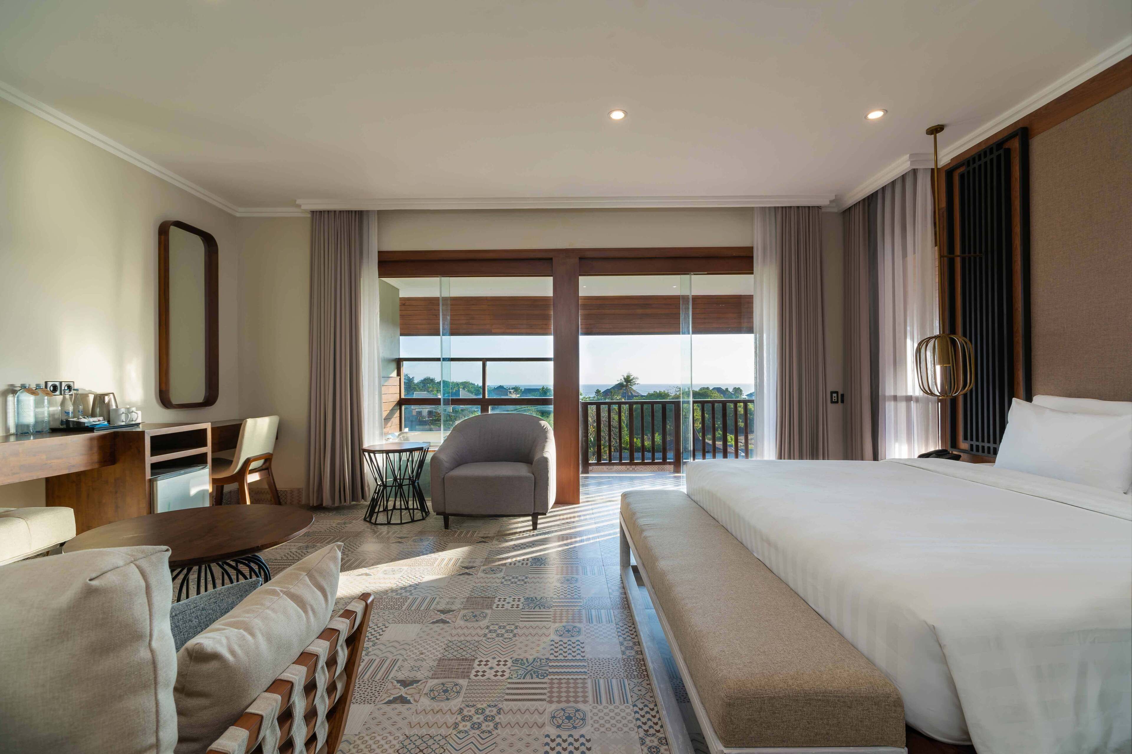 A hotel room with a large bed, a sofa, a desk, and a balcony with a view.
