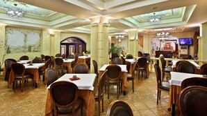 Un comedor amplio con varias mesas y sillas, una araña y un mural en la pared.