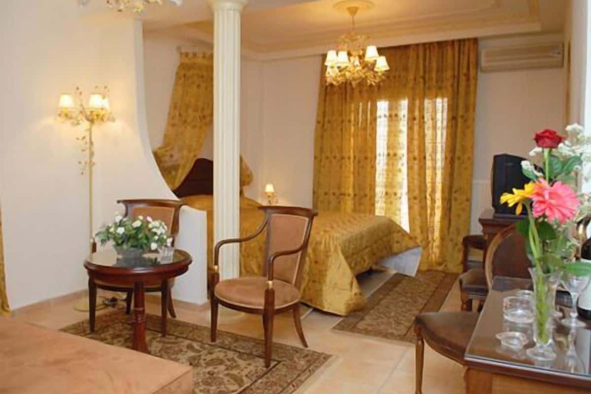 Habitación de hotel con cama, zona de estar con mesa y sillas, candelabro y televisor.