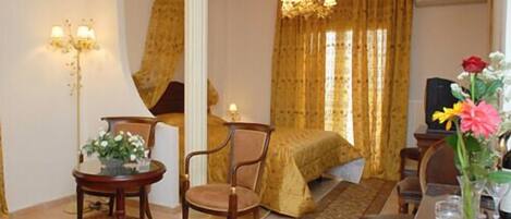 A hotel room with a bed, a sitting area with a table and chairs, a chandelier, and a television.
