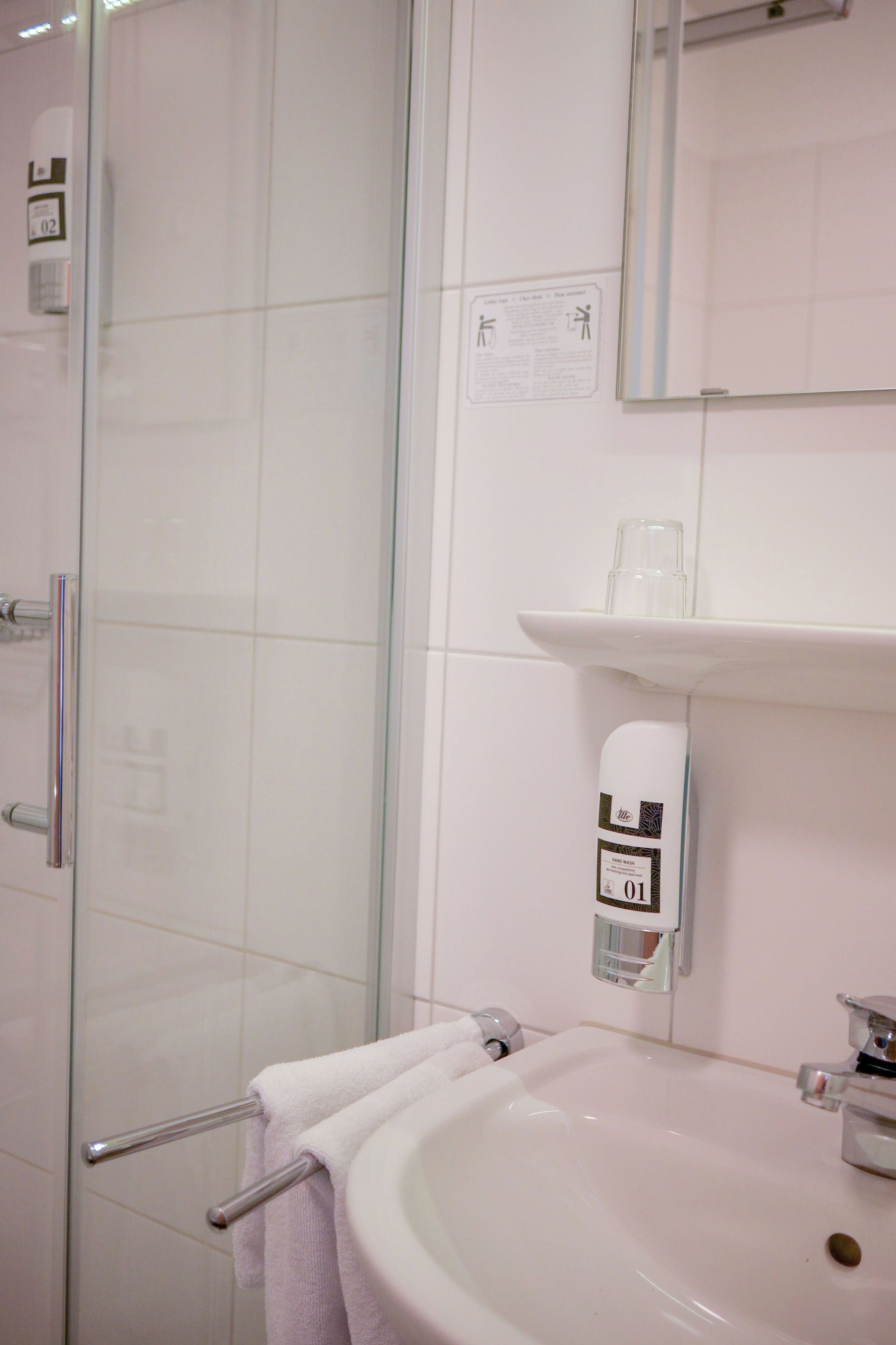 A bathroom with a glass shower enclosure, a white sink, and a soap dispenser.