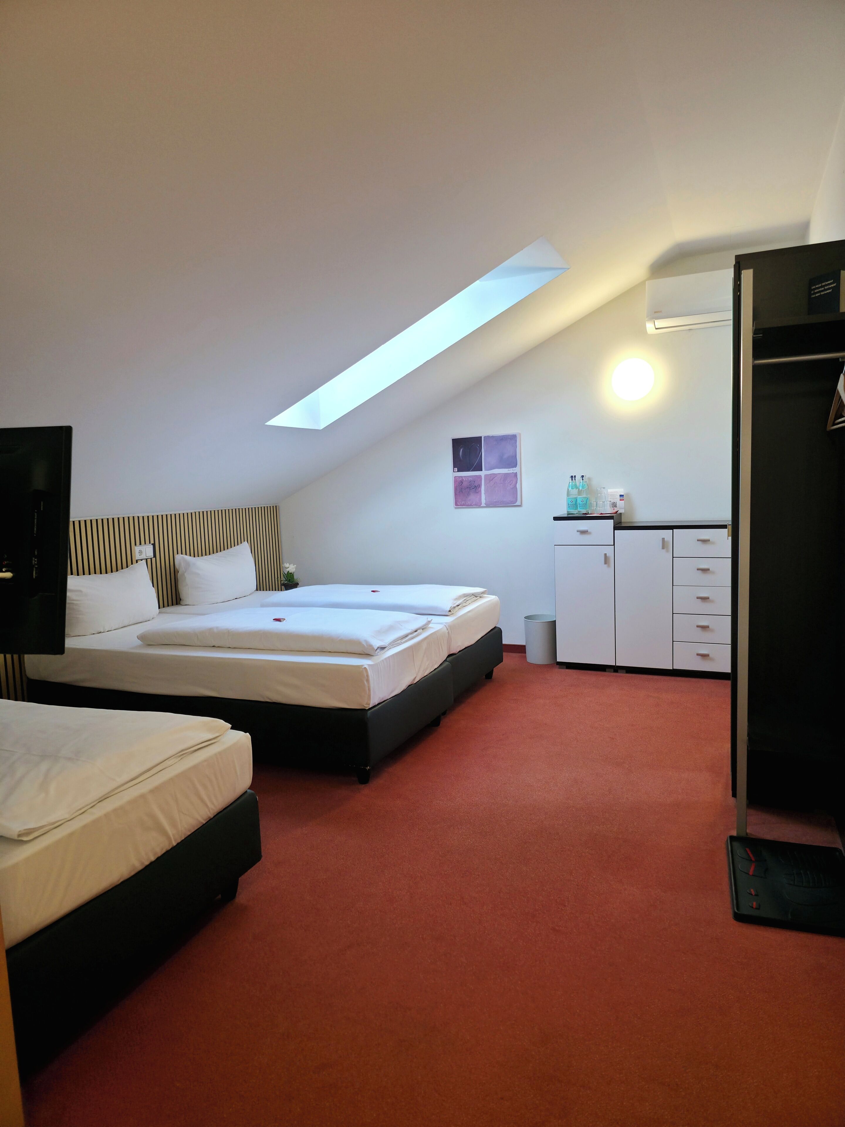 Een hotelkamer met twee bedden, een bureau, een kledingkast en een dakraam.
