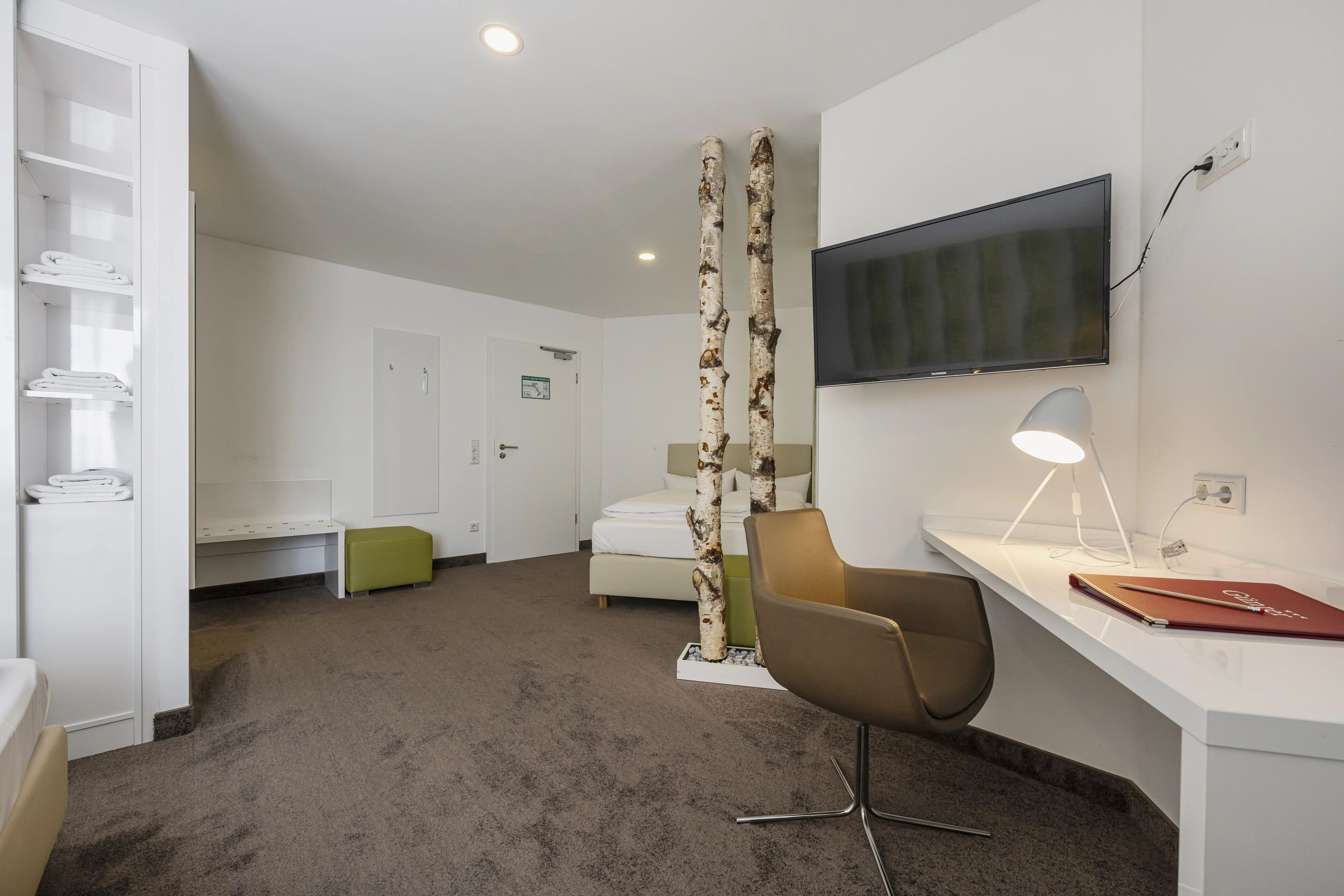 A modern hotel room with a desk, chair, television, and a bed.