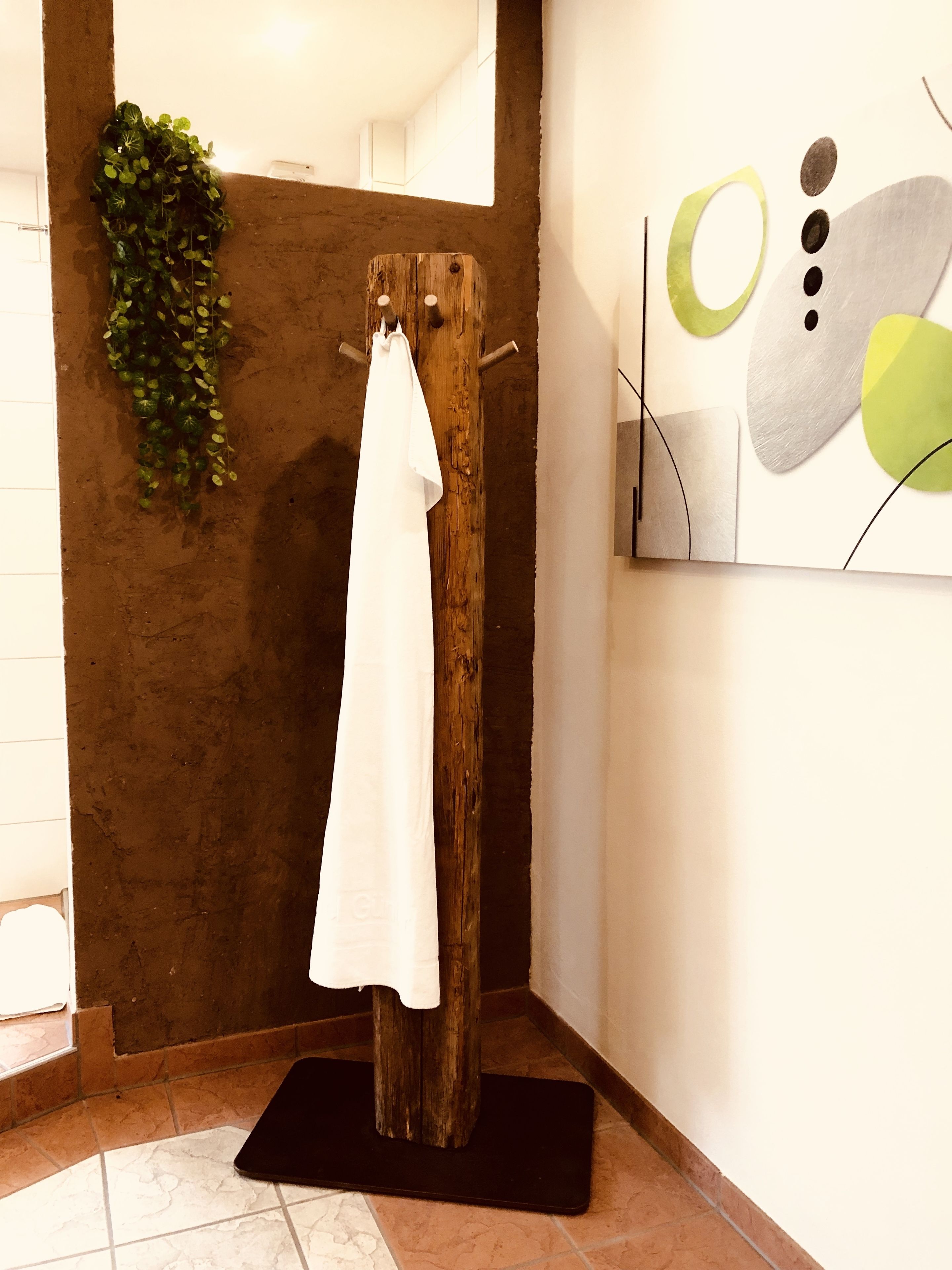 A room with a wooden towel rack, a green plant, and a modern abstract painting.