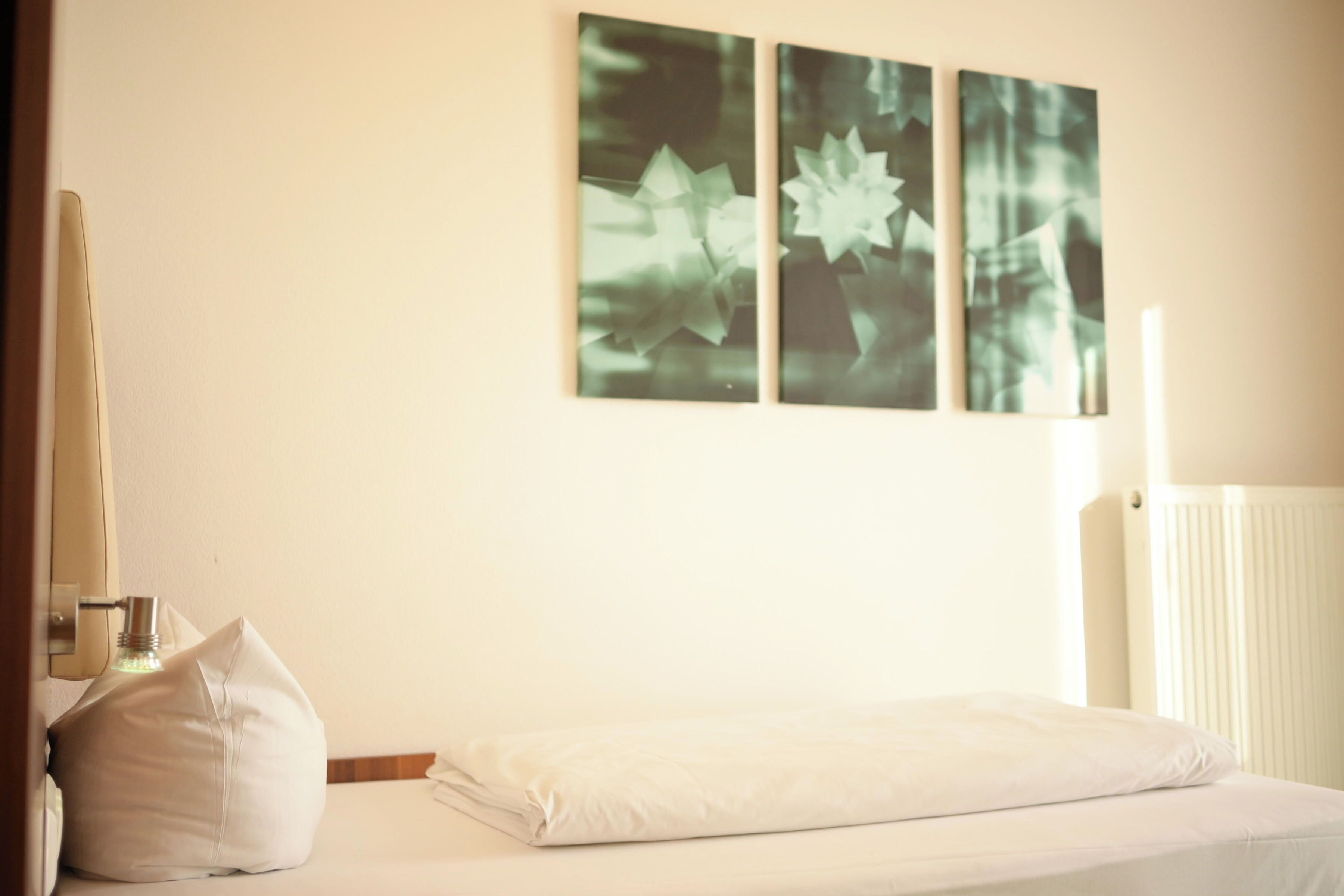 Una habitación de hotel con una cama, un almohadón, una botella y tres cuadros colgados en la pared.