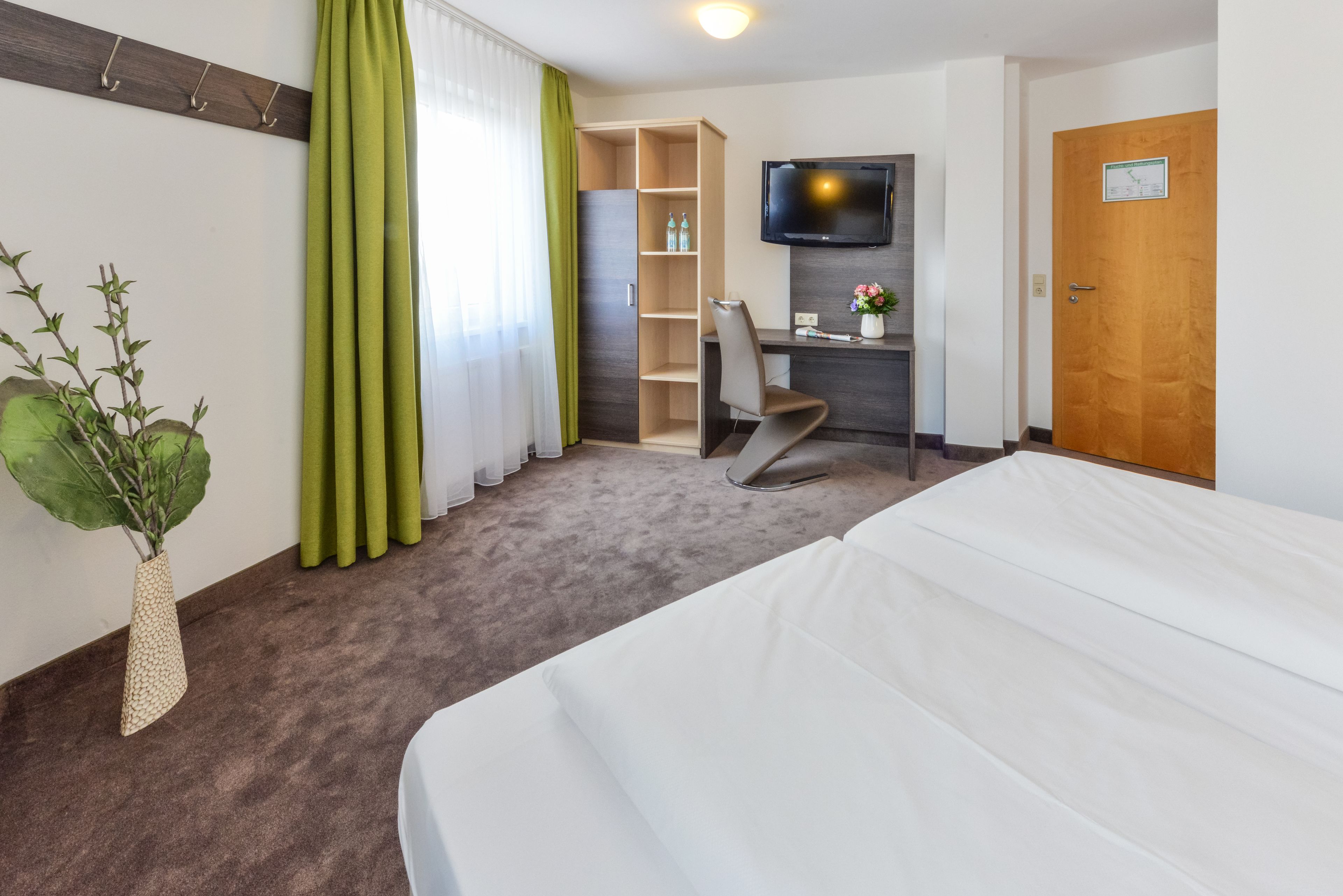 Una habitación de hotel con cama, escritorio, silla, televisor y planta.