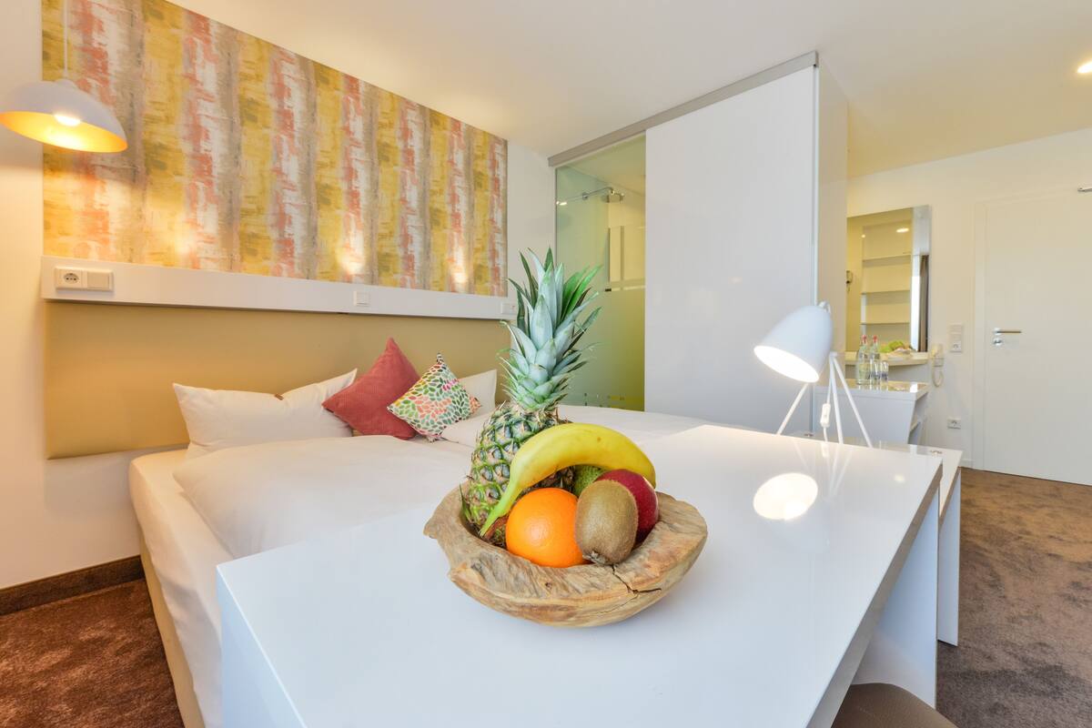 Habitación de hotel con cama, frutero en la mesita de noche, lámpara y un cuadro en la pared.