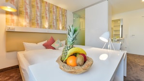 Habitación de hotel con cama, frutero en la mesita de noche, lámpara y un cuadro en la pared.