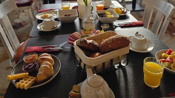 Un desayuno con una mesa dispuesta para dos personas, que incluye croissants, gofres y una tetera.