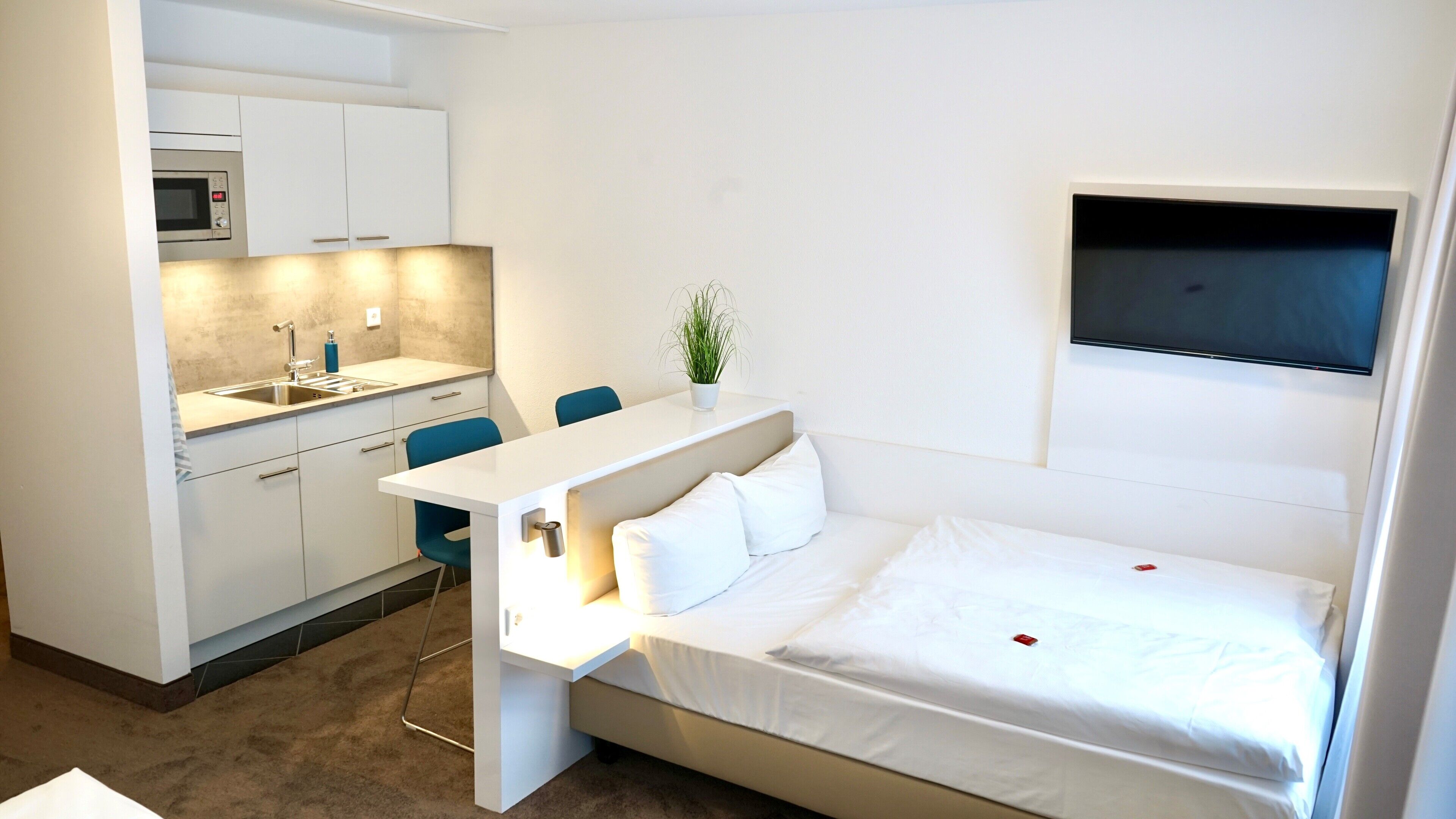 A compact hotel room with a kitchenette, a bed, a TV, and a small seating area.