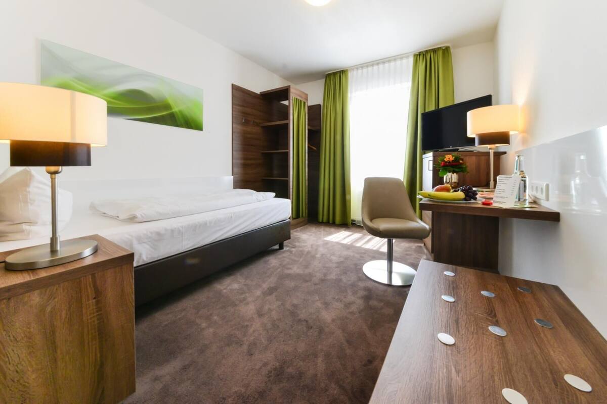 Habitación de hotel con cama, escritorio con silla, televisor y cortina verde.