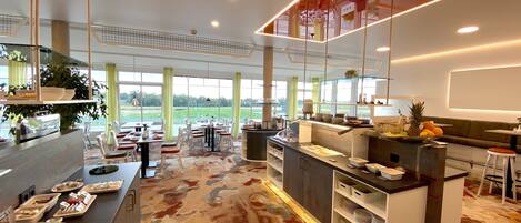 A modern hotel restaurant with a central counter, dining tables, and chairs.