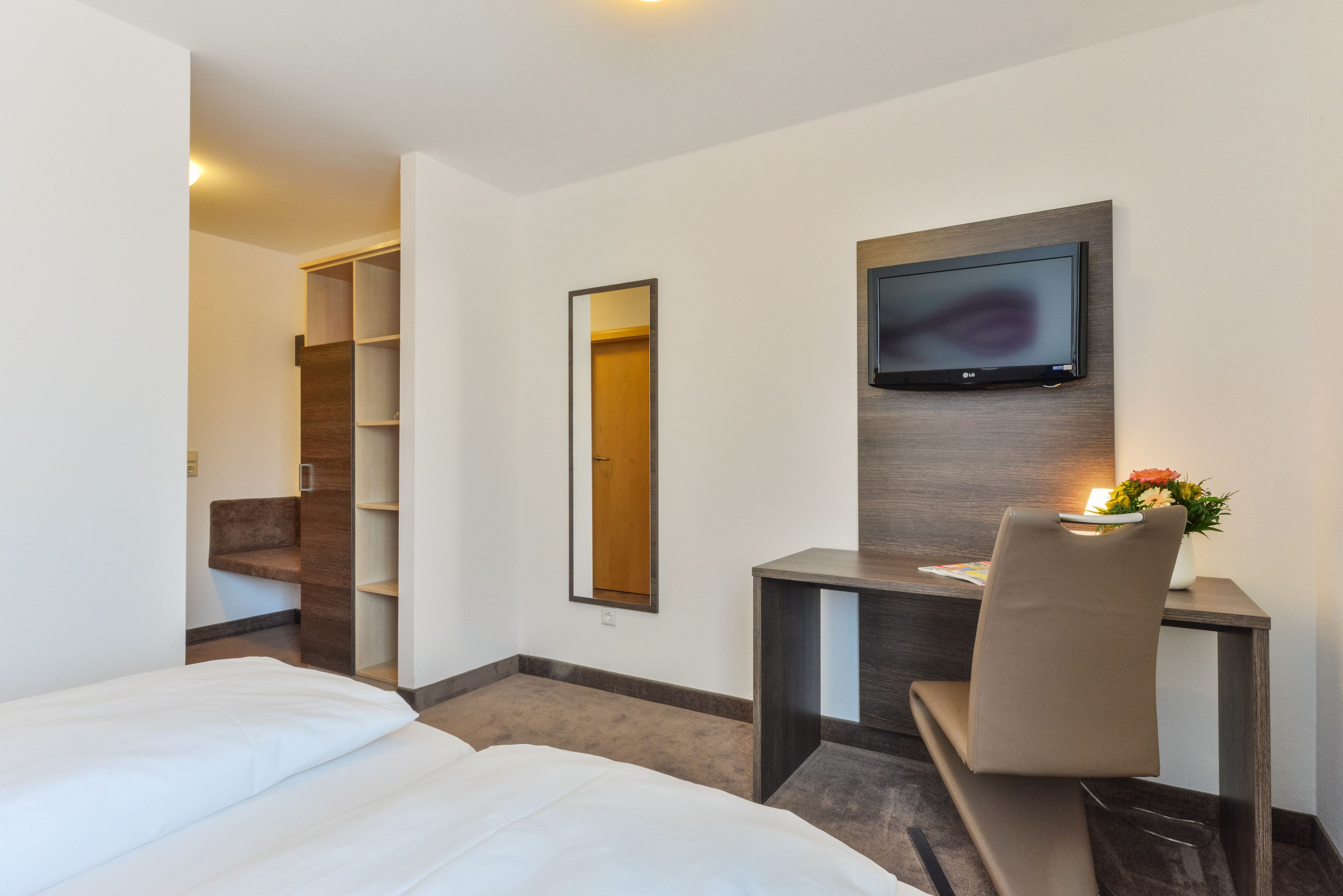 Habitación de hotel con dos camas, un escritorio con silla, televisor montado en la pared y un espejo.