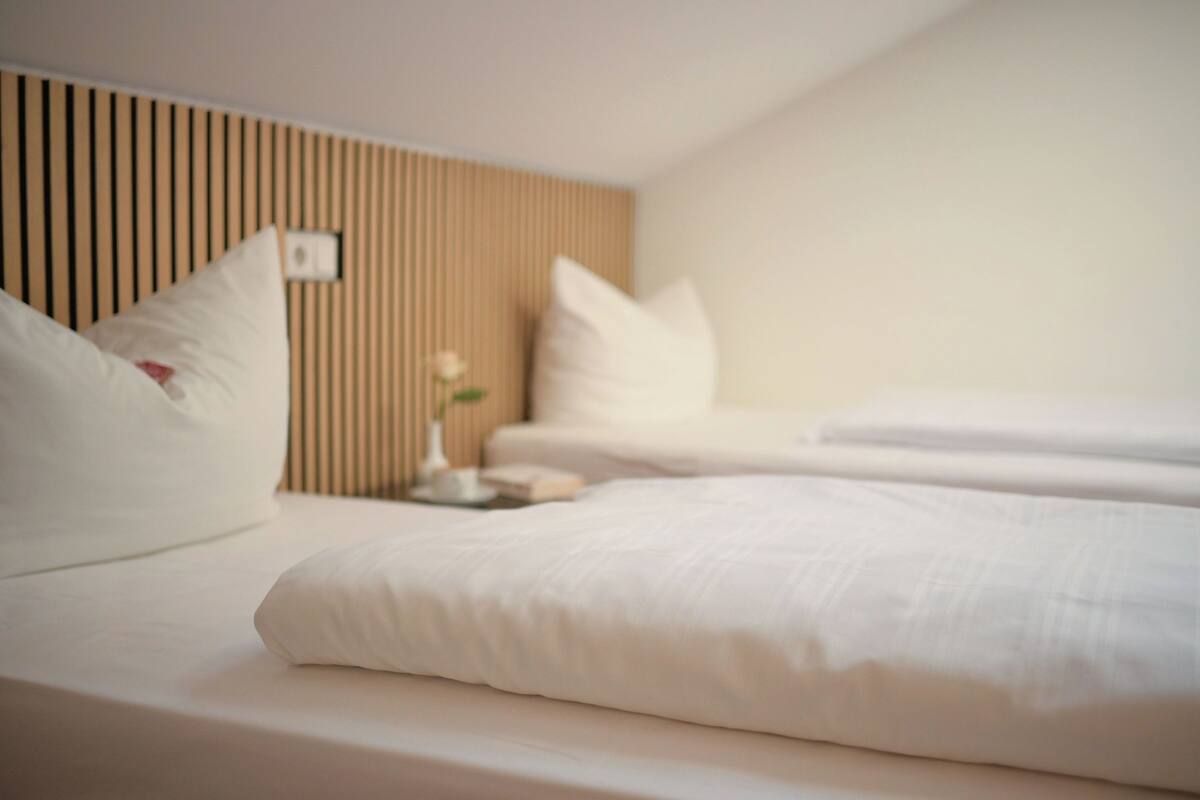 Una habitación de hotel con cama, almohadas, una mesita de noche y un interruptor de luz en la pared.