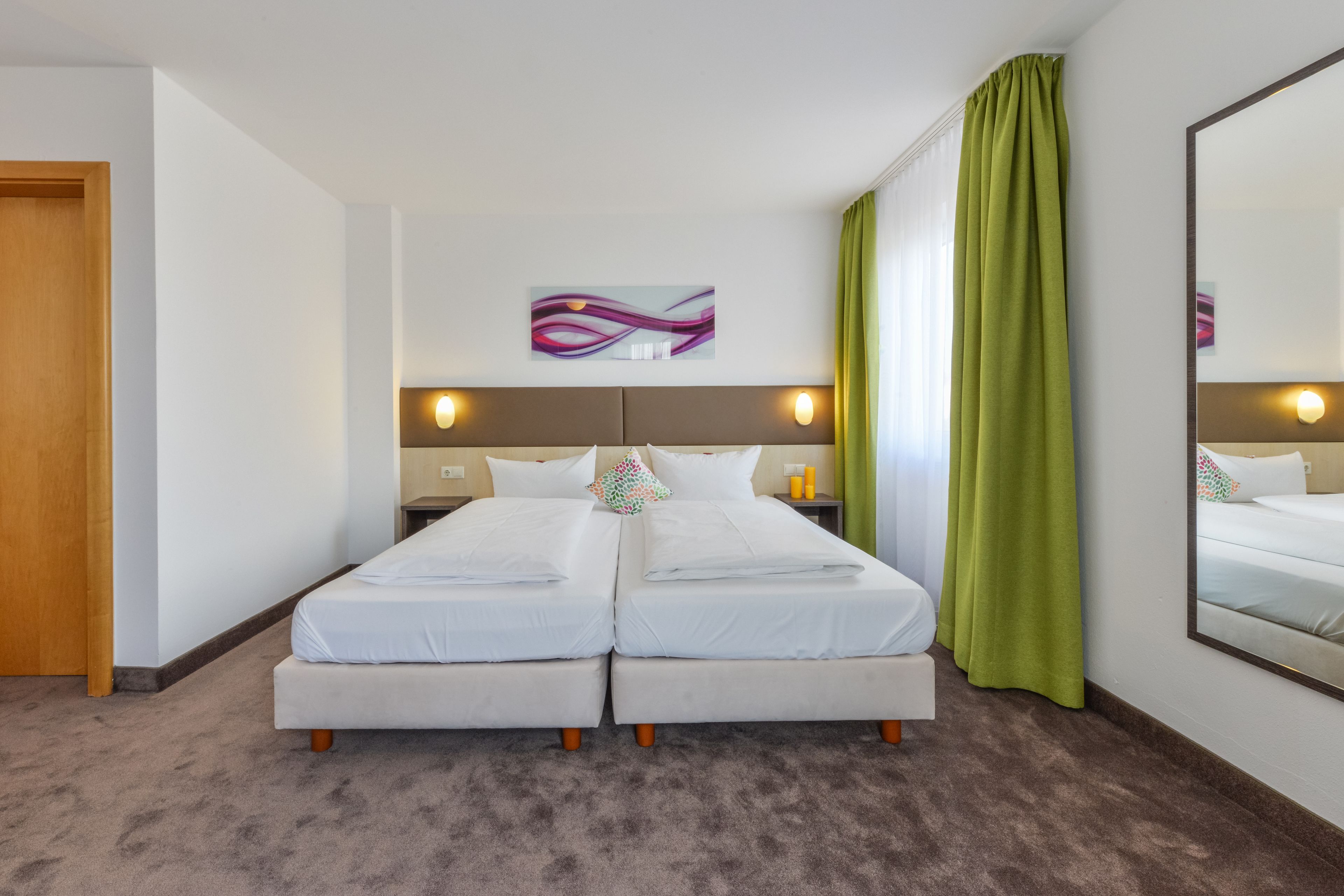 A double bed with two pillows, a nightstand, a mirror, and a painting on the wall.